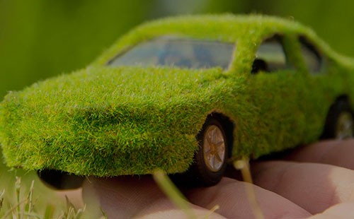 une main tenant une petite voiture couverte d'herbe
