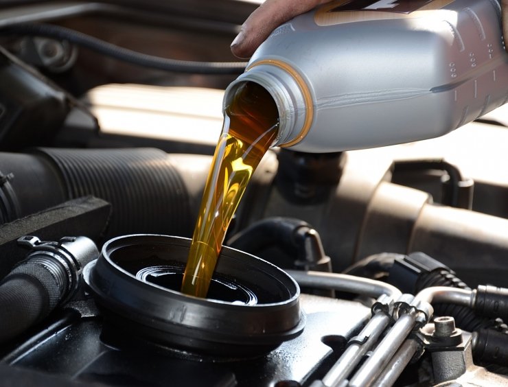 une personne qui verse de l'huile dans un moteur de voiture